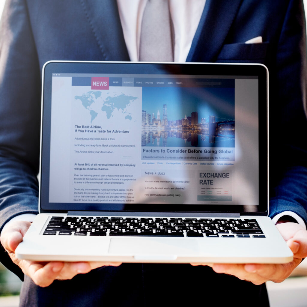 Person holding a laptop displaying website homepage and digital news content